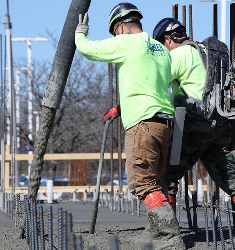 Two concrete construction workers pumping concrete