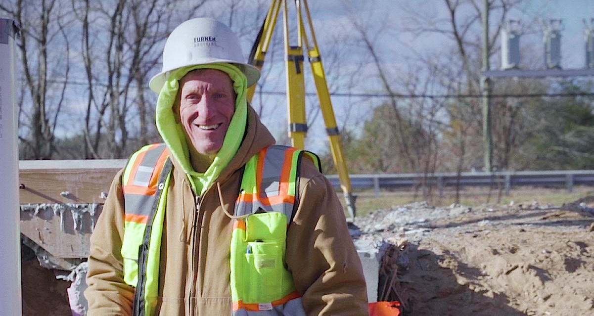 A Turner Brothers employee stands smiling in front of total station